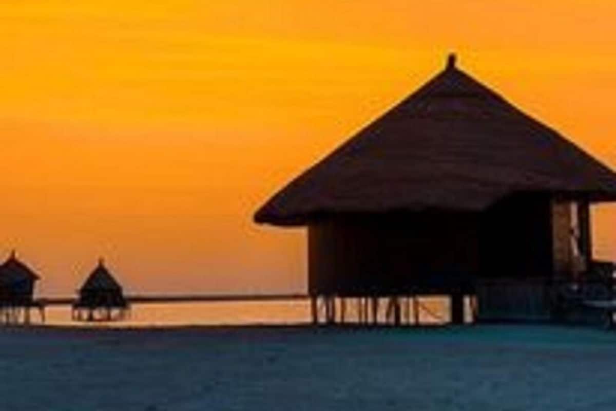 Ein überwasserbungalow am Strand mit einem Reetdach, verbunden durch eine Holzterrasse.