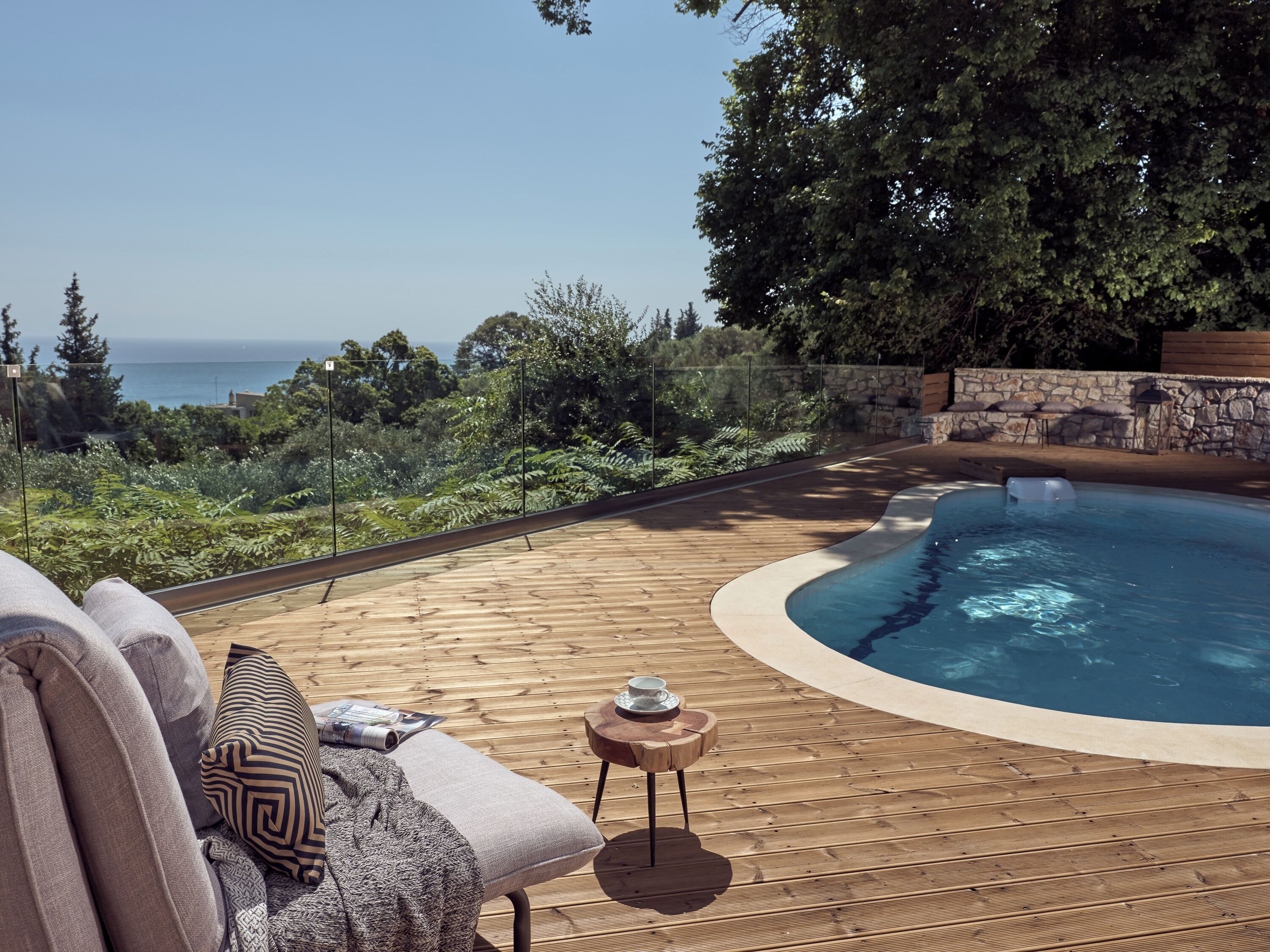 Un patio in legno con una piscina a forma curva, mobili da esterno e vista sul mare.