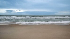 A beach with waves approaching the shore under a cloudy sky.