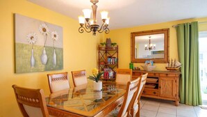 A dining area with a glass-top table, wooden chairs, a chandelier, a bookshelf, and a mirror.