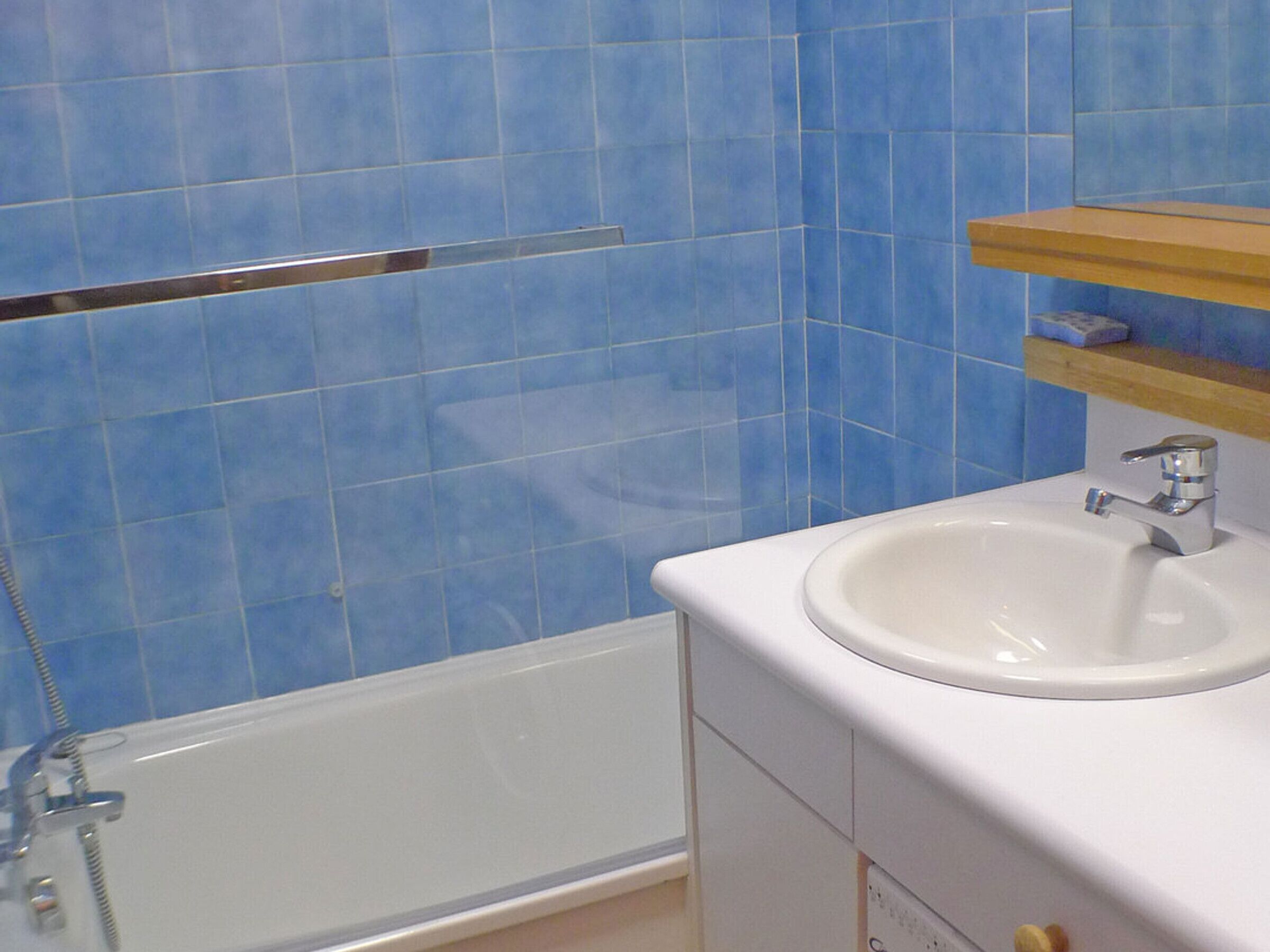 Un baño con una bañera, un lavamanos blanco y azulejos azules.
