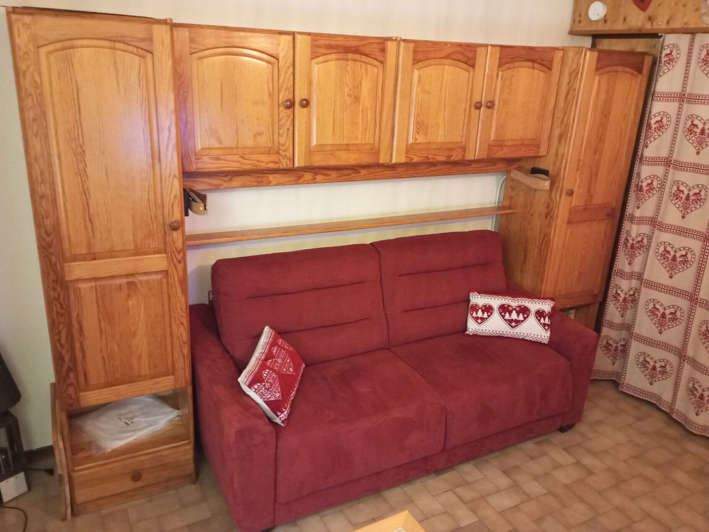 A red sofa with heart-patterned pillows, wooden cabinets, and a patterned curtain.