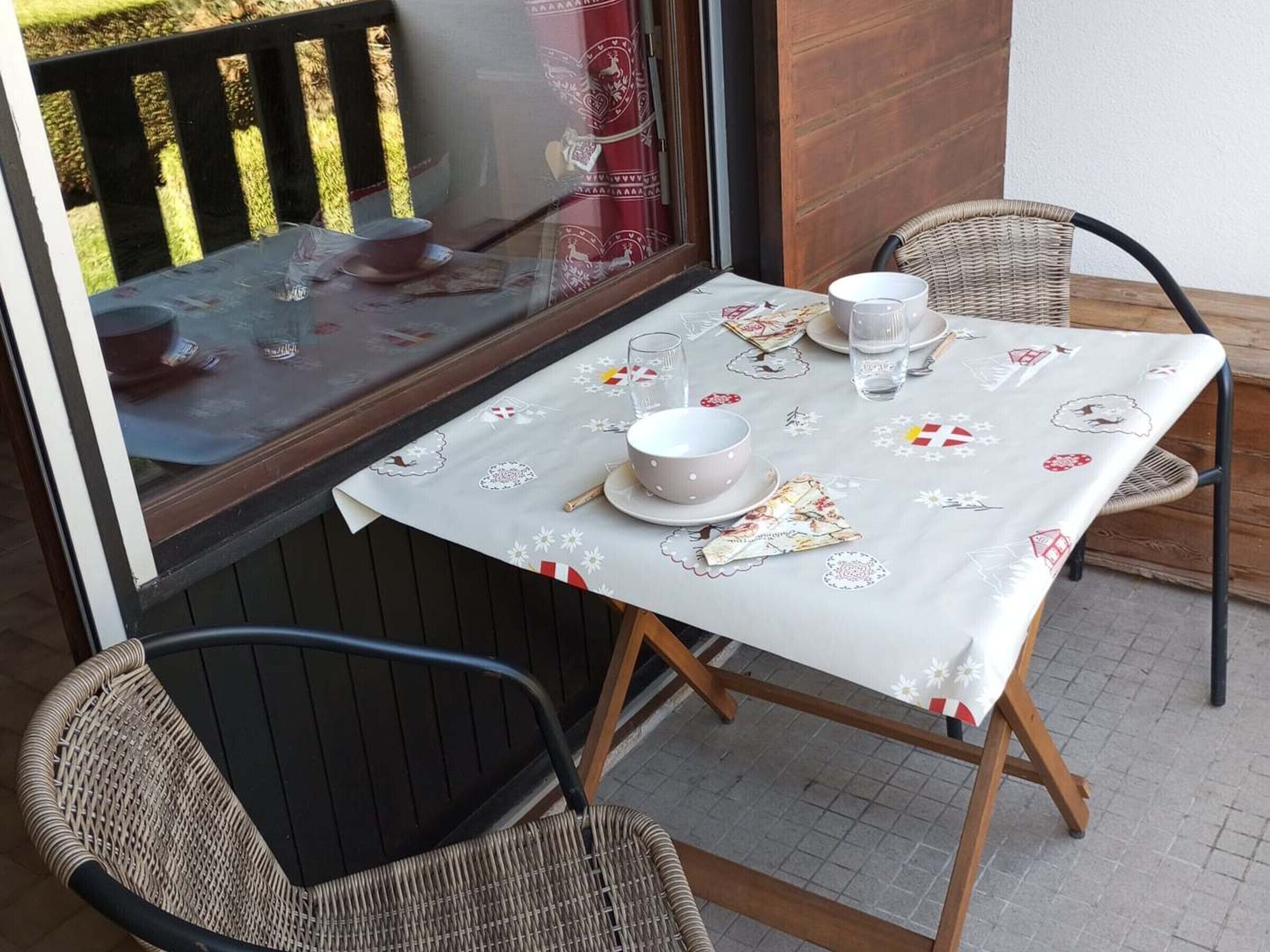 A table set for two with a white tablecloth, two chairs, and a window with a view of trees.