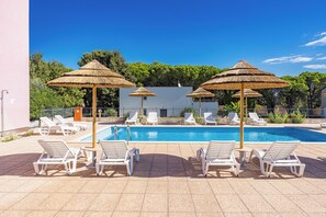 A swimming pool with sun loungers and thatched umbrellas, surrounded by trees and a building. - Residence Kamenjak Runke (Medulin)