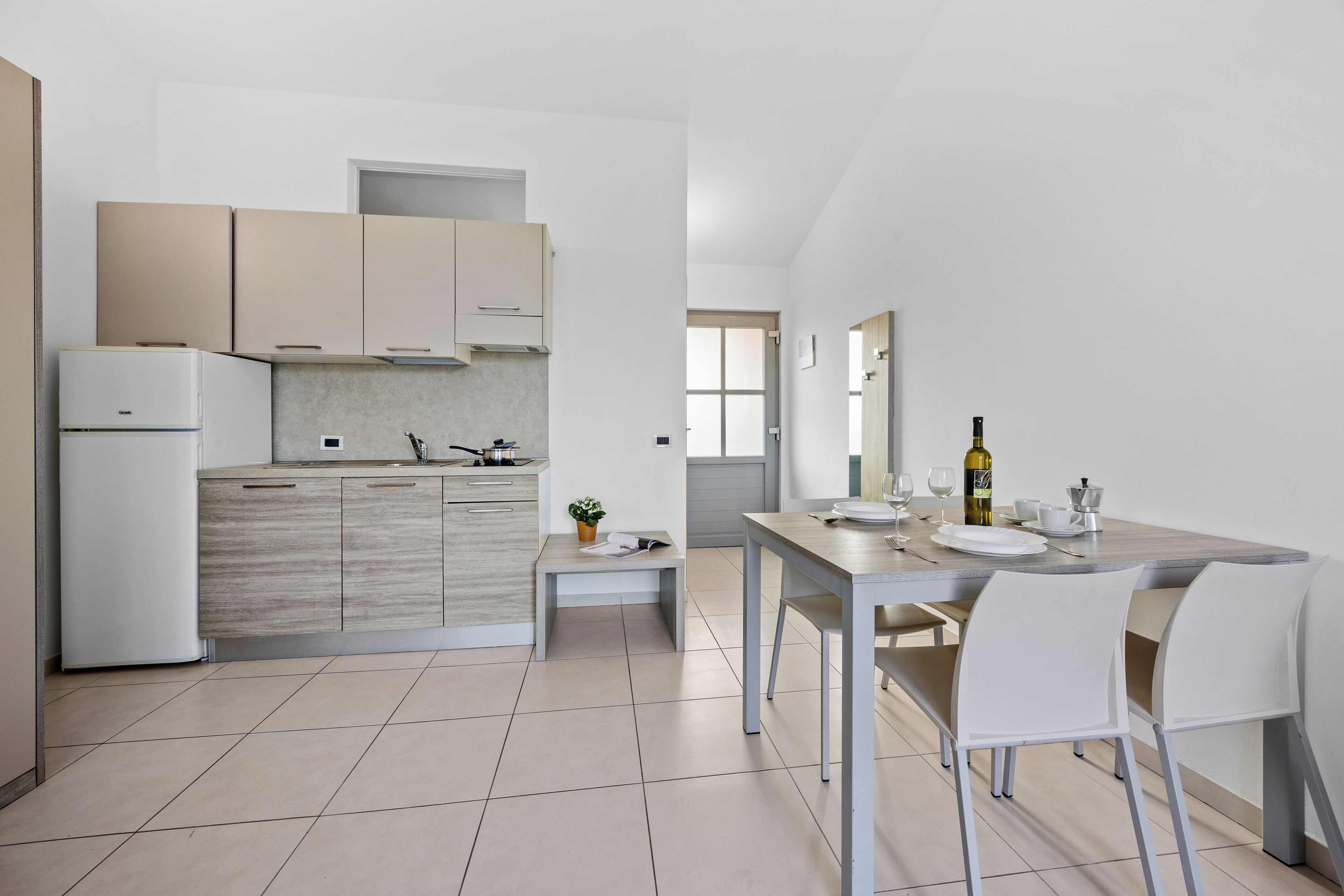 Una cocina moderna con armarios de madera clara, horno integrado y comedor con mesa y sillas.