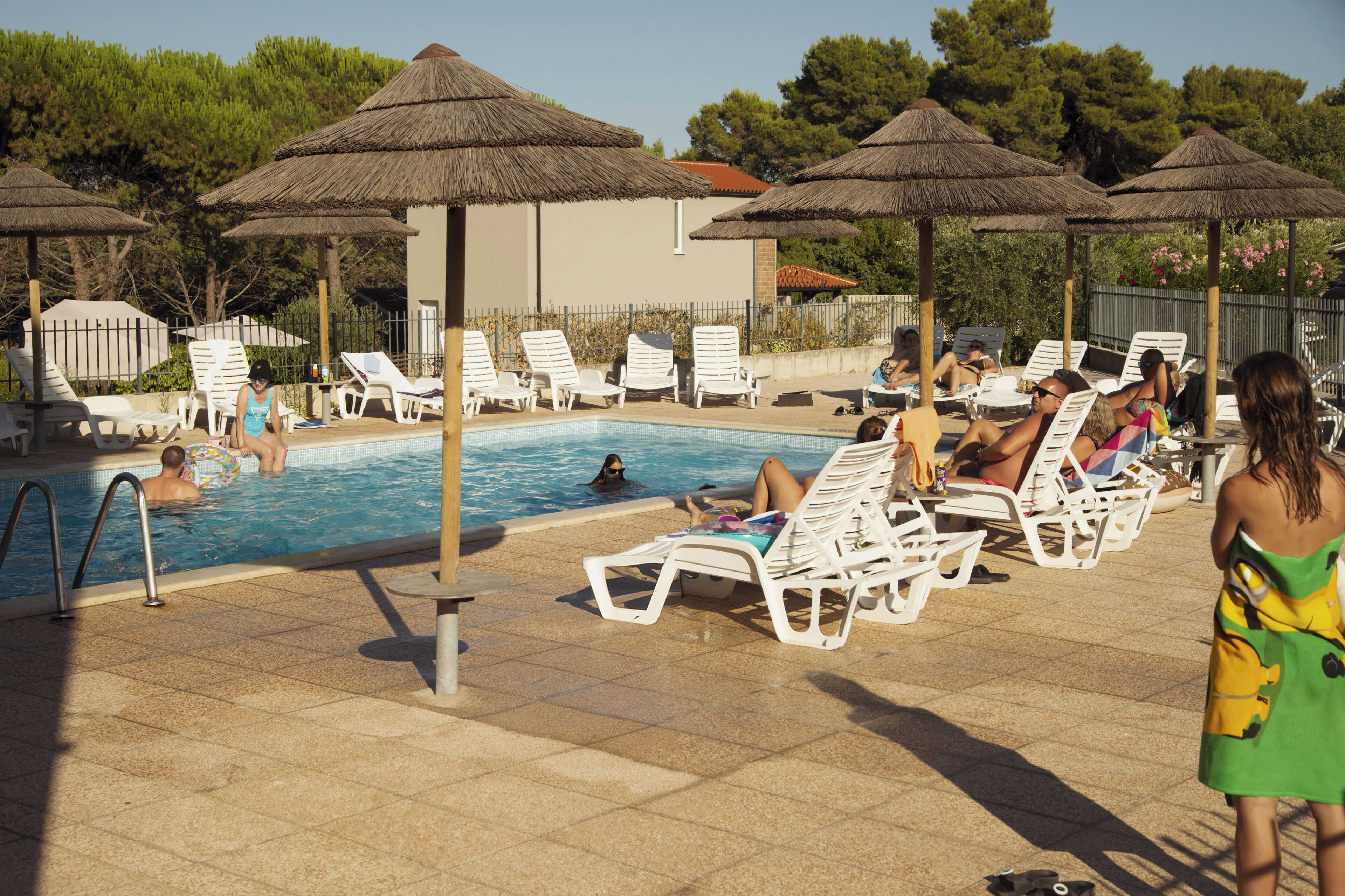 Un área junto a la piscina con sillas de descanso, sombrillas y una piscina.