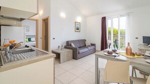 Una cocina moderna con un lavamanos, una zona de comedor con mesa y sillas, un sofá y un ventanal con cortinas.