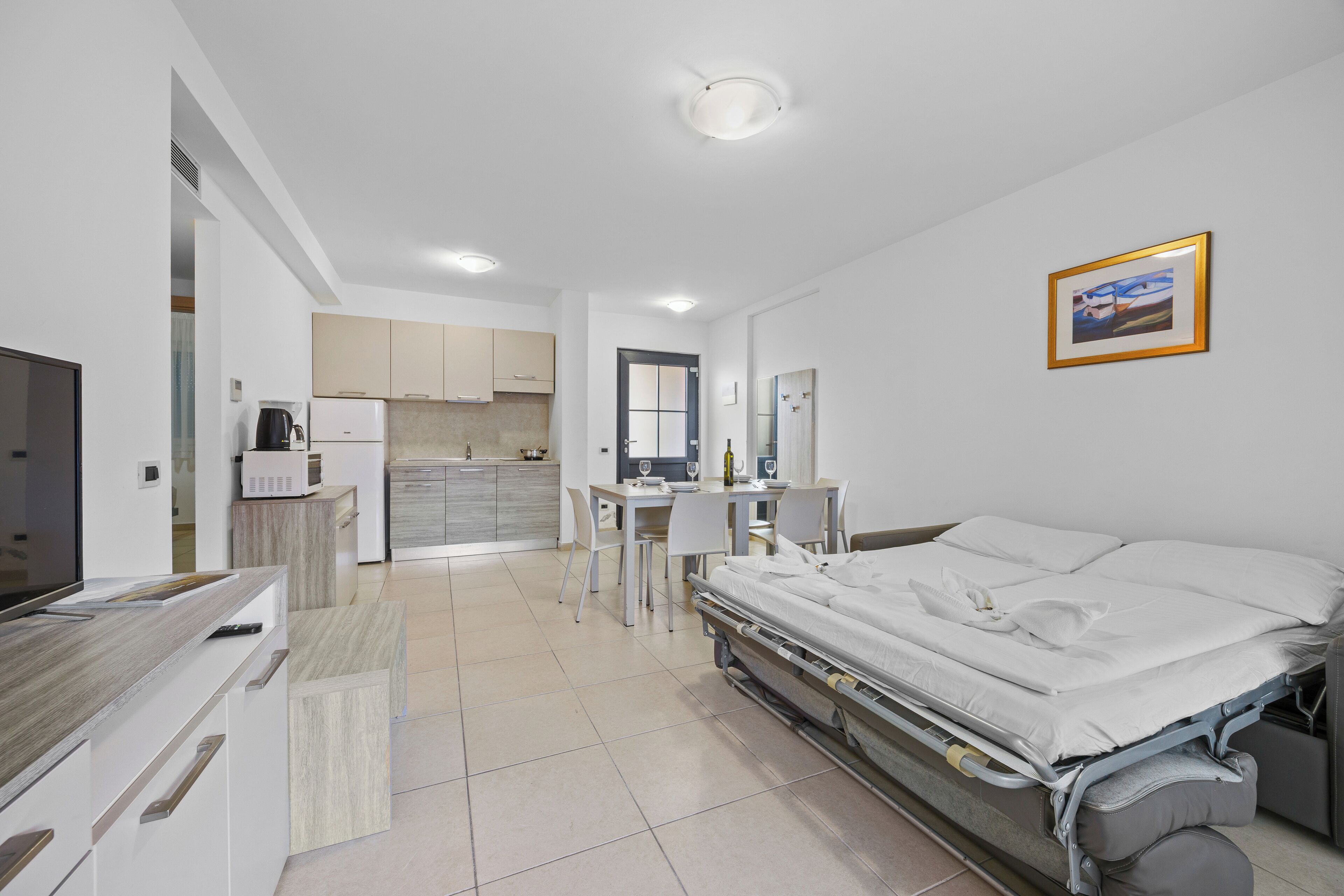 A modern hotel room with a bed, bedside table, and a view of the kitchen area.
