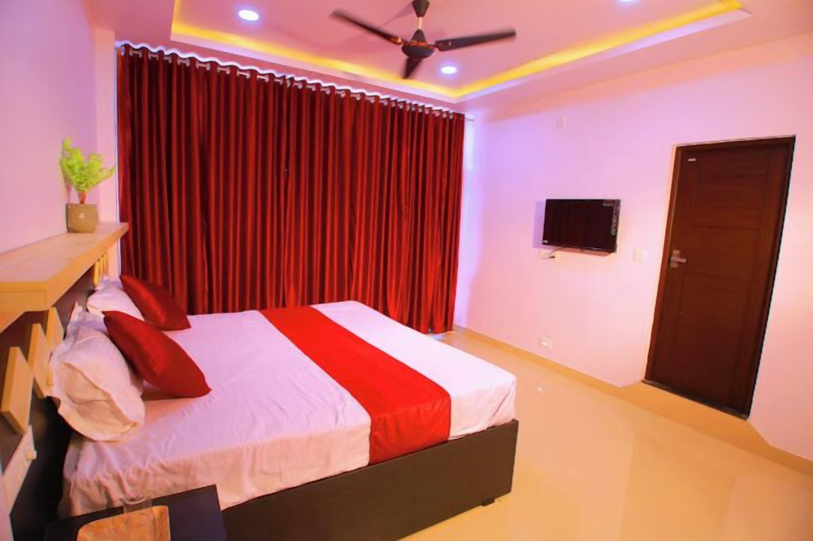 A bedroom with a bed, a ceiling fan, a TV, and a door.