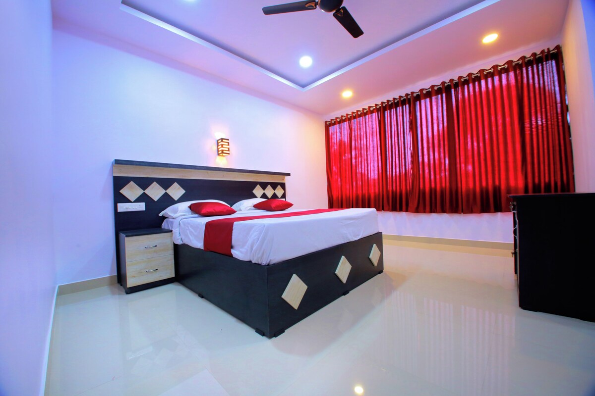 Une chambre à coucher avec un lit, une table de chevet, un ventilateur de plafond et une fenêtre avec des rideaux rouges.