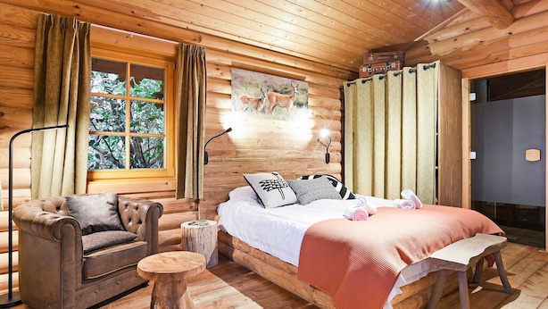 Une chambre confortable, aménagée dans un chalet en bois, avec un lit, une chaise, une petite table et une fenêtre avec des rideaux.
