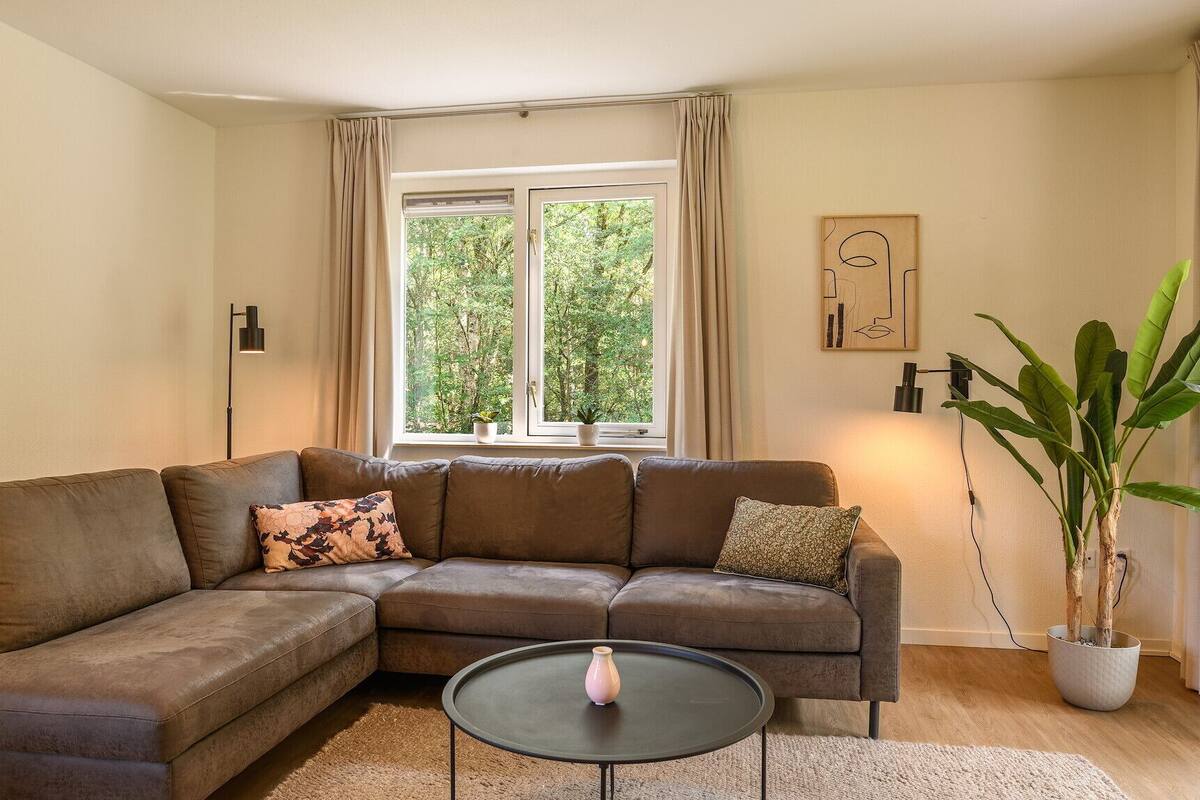 A modern living room with a brown sectional sofa, a round coffee table, and a large window with curtains.