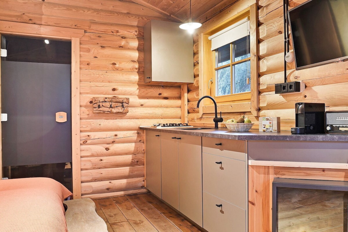 A compact log cabin room with a kitchenette, a bed, and a window with a view.