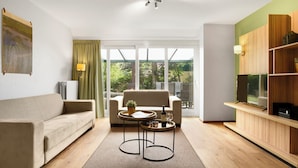 Un salon moderne avec un canapé, une table basse, un fauteuil et un téléviseur posé sur une étagère en bois.