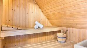 Puisesta laudasta rakennettu sauna, jossa on rullalle kelattuja pyyhkeitä ja puinen ämpäri.