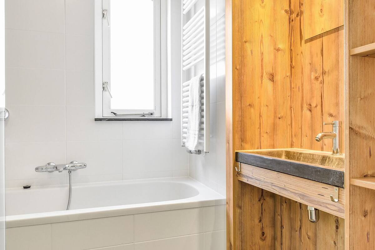 A bathroom with a white bathtub, a window, and a wooden vanity with a sink.
