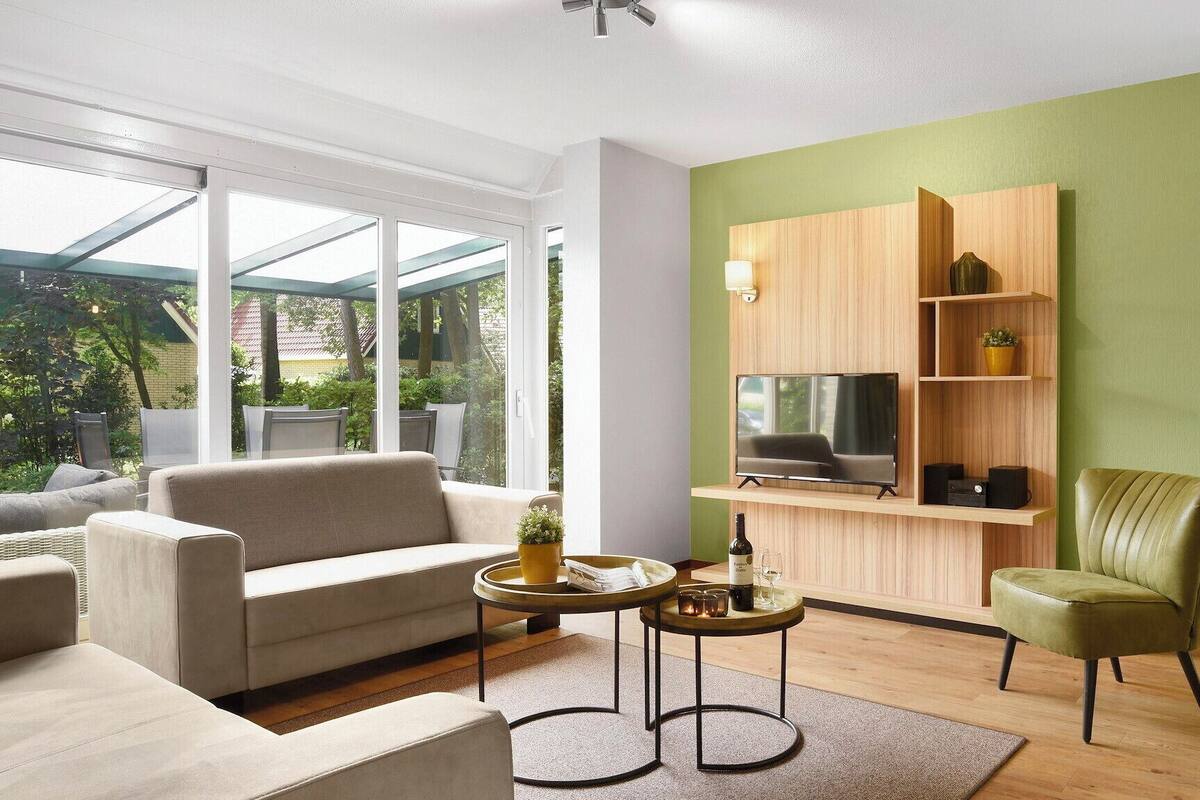 A modern living room with a sofa, a green armchair, a coffee table, and a TV mounted on a wooden wall.