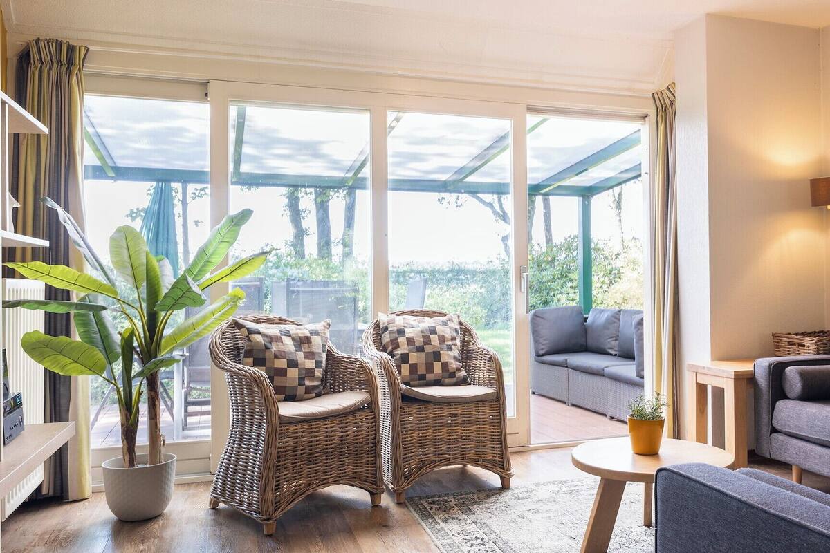 A spacious living room with a large sliding glass door leading to an outdoor area, wicker chairs, a grey sofa, and a small table with a plant.