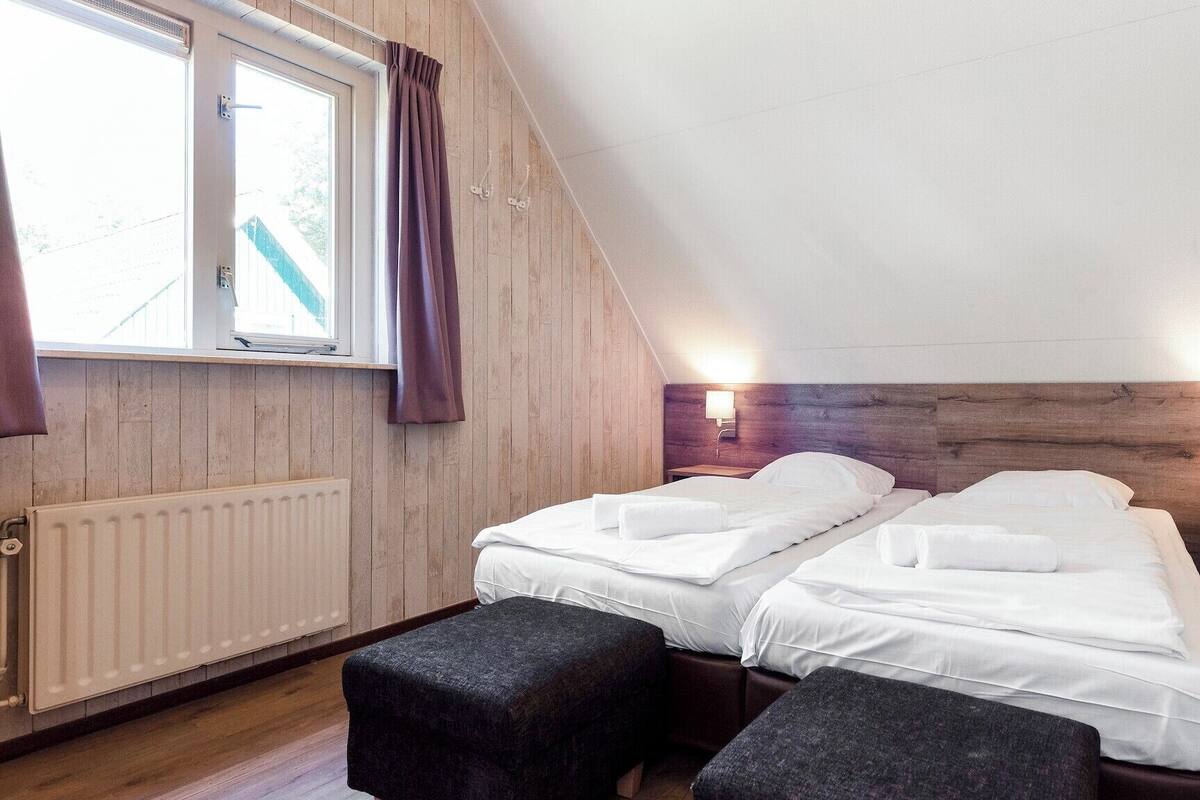 A room with two beds, a window with curtains, a radiator, and two wall-mounted lights.