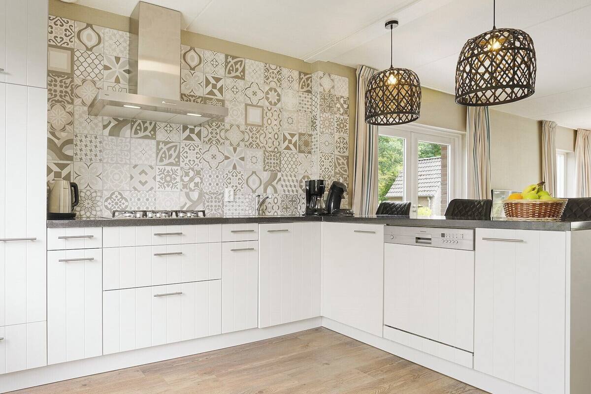 A modern kitchen with white cabinetry, patterned backsplash, and two hanging pendant lights.