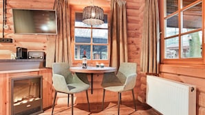 L’intérieur chaleureux d’un chalet, avec un décor en bois, une table à manger avec des chaises, un téléviseur et une cheminée.