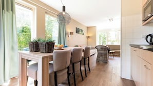 Une cuisine moderne avec un coin repas, un plancher en bois et de grandes fenêtres donnant sur un paysage verdoyant.