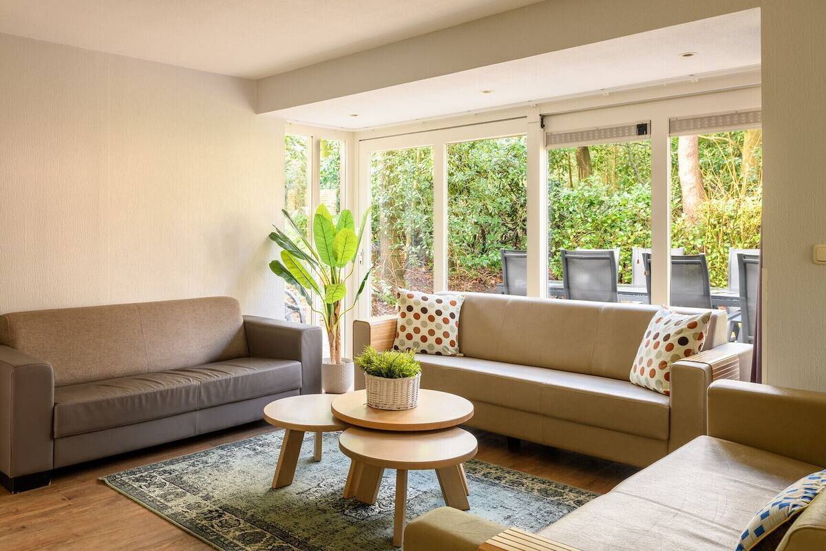 A living room with a grey sofa, a coffee table, and a large window with a view of greenery.