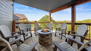 A covered deck with Adirondack chairs, a stone fire pit, and a view of the landscape. - Private Pool! Rustic Charm! Steps from the Lake! (Branson)