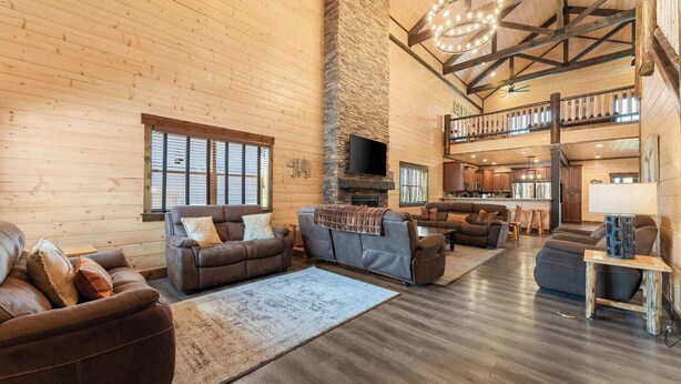 A spacious living area with a fireplace, multiple seating options, and a kitchen in the background. - Private Pool! Rustic Charm! Steps from the Lake! (Branson)