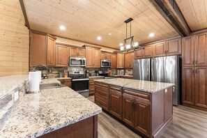 A kitchen with wooden cabinets, granite countertops, stainless steel appliances, and a hanging light fixture. - Private Pool! Rustic Charm! Steps from the Lake! (Branson)