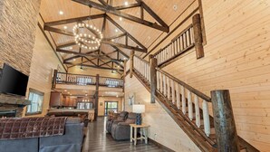 A spacious living area with a wooden staircase, a fireplace, and a television. - Private Pool! Rustic Charm! Steps from the Lake! (Branson)