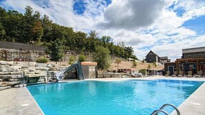 A swimming pool with a slide, stone walls, and a building with a sloped roof. - Private Pool! Rustic Charm! Steps from the Lake! (Branson)