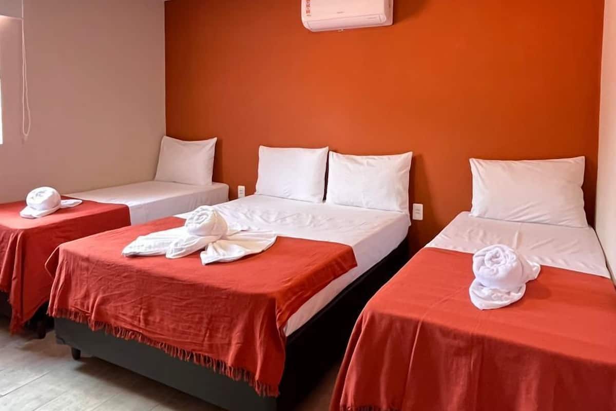Ein Hotelzimmer mit zwei Betten, beide mit roter Bettdecke und weißen Kissen. Eine Klimaanlage ist an der Wand oberhalb der Betten angebracht.