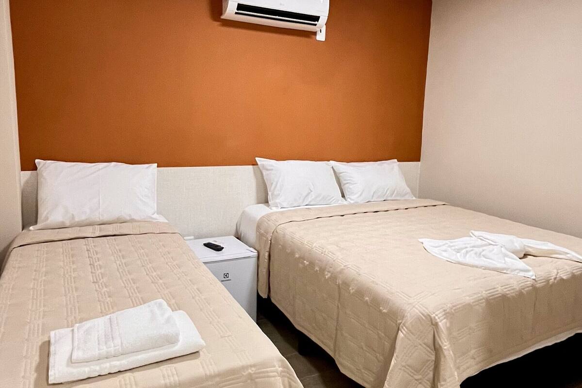Ein Hotelzimmer mit zwei Betten, einem Nachttisch, einer Klimaanlage und einem gefliesten Boden.