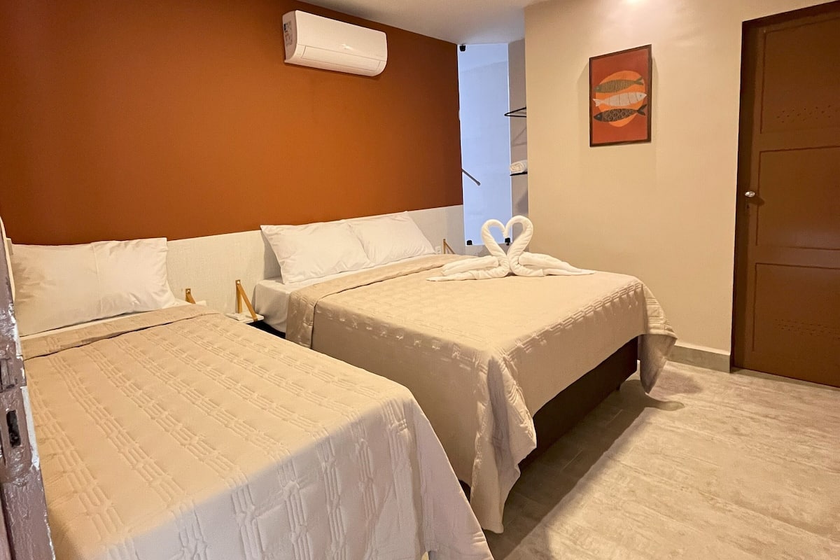 Ein Hotelzimmer mit zwei Betten, einer Wandklimaanlage, einem gerahmten Kunstwerk und einer Tür.