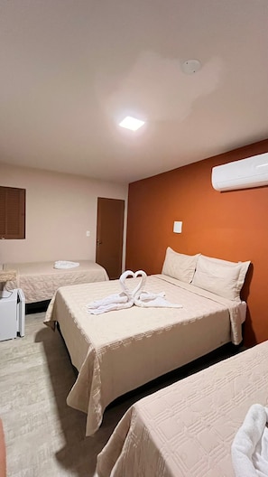 Habitación de hotel con dos camas, una mesita de noche y un aire acondicionado en la pared.