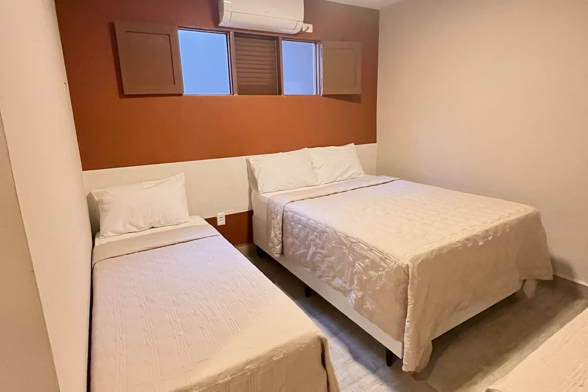 Ein Hotelzimmer mit zwei Betten, einem Fenster mit Jalousien, einer Klimaanlage und einem gefliesten Boden.
