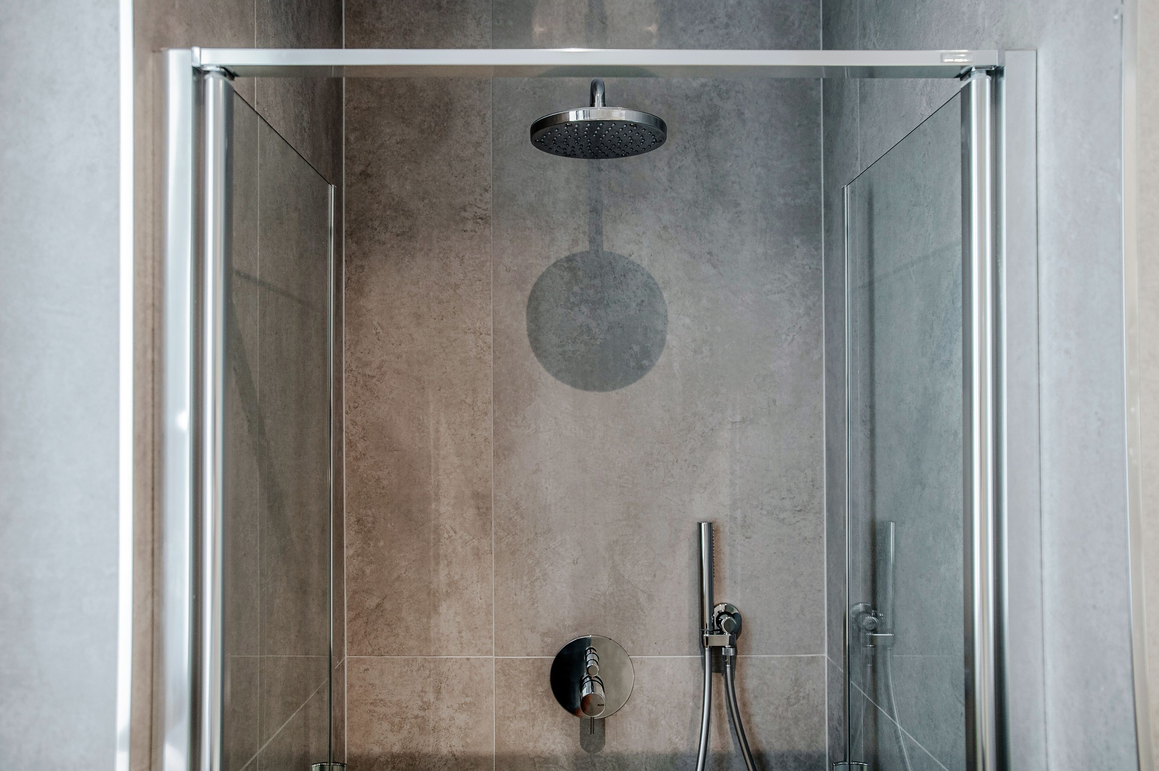 A modern shower enclosure with a glass door, a handheld showerhead, and a wall-mounted control panel.