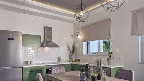 A modern kitchen with green cabinets, a stainless steel refrigerator, a wooden dining table with chairs, and pendant lighting.