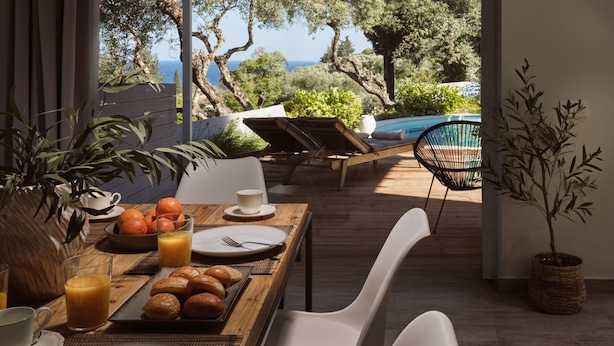 A breakfast table with orange juice, pastries, and a view of a pool and trees.