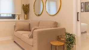 A modern living room with a beige sofa, two gold-framed mirrors, a small round wooden table, and a potted plant. - Retiro: Comfortable flat in the area of Delicias (Madrid)