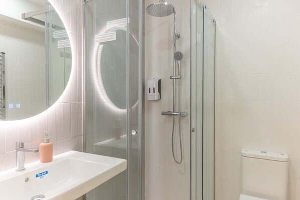 A modern bathroom with a glass-enclosed shower, a white sink with a soap dispenser, and a mirror with a circular frame.