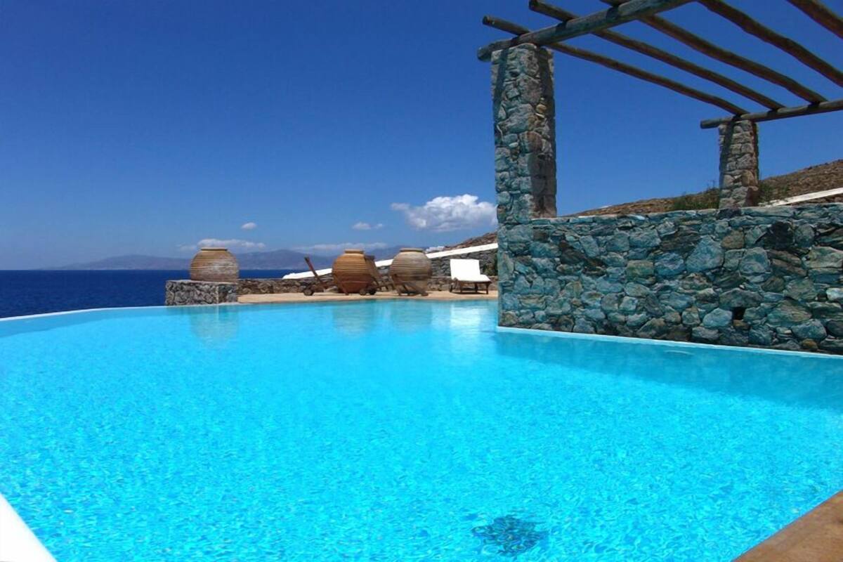 Une piscine aux eaux d’un bleu limpide, bordée de murs en pierre et surmontée d’une pergola.