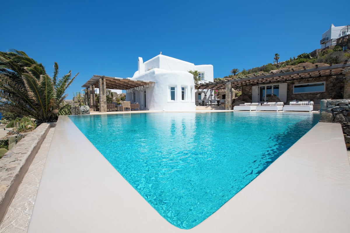Une villa moderne dotée d’une piscine, de murs en pierre et d’une pergola.