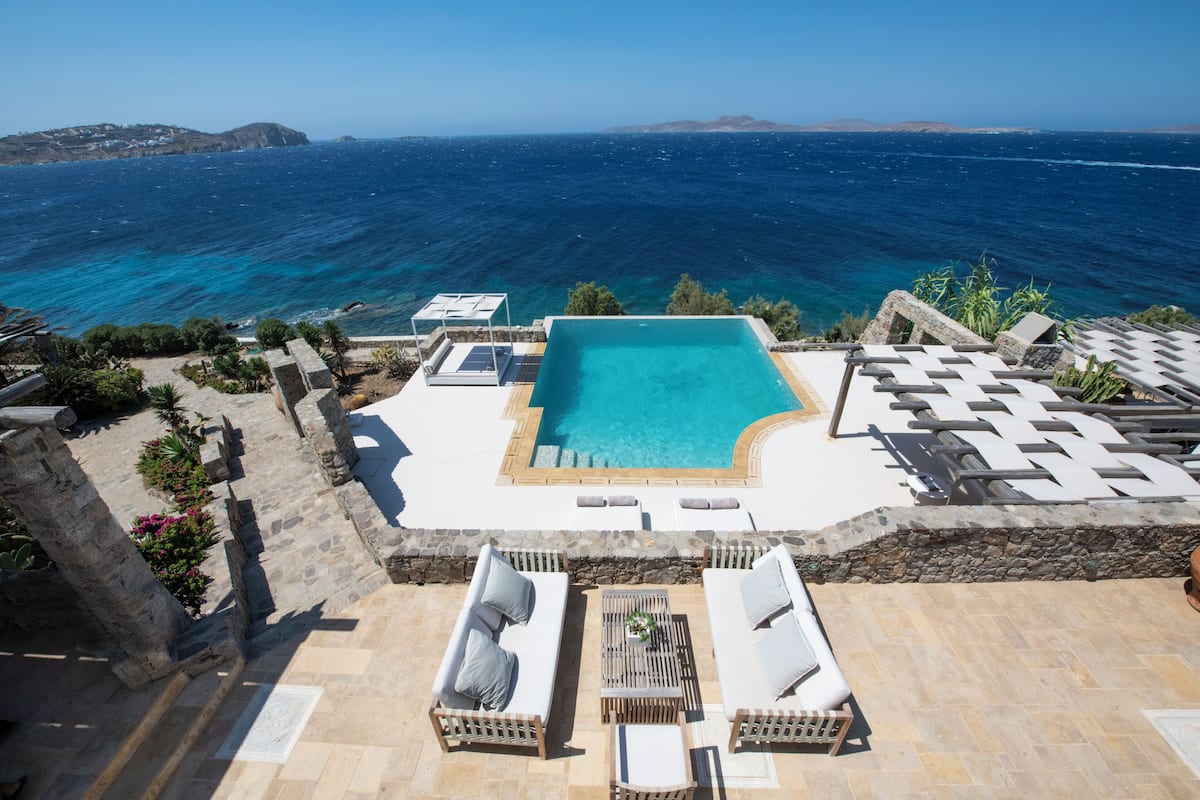 Une piscine à débordement offrant une vue dégagée sur la mer, un espace salon extérieur et un chemin en pierre.