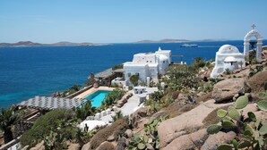 A white building with a pool, surrounded by cacti and rocks, overlooking the sea. - Topos Exclusive Mykonos  (Mykonos)