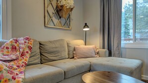 A living room with a grey sofa, a wooden coffee table, a floor lamp, and a window with curtains.