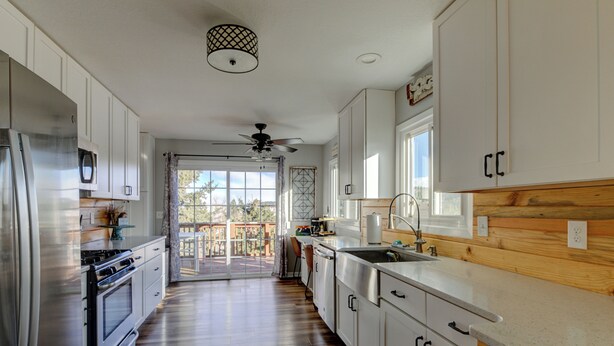 A modern kitchen with white cabinets, stainless steel appliances, and a wooden accent wall.