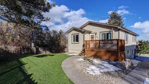 A two-story house with a fenced backyard, a wooden deck, and a wheelbarrow.