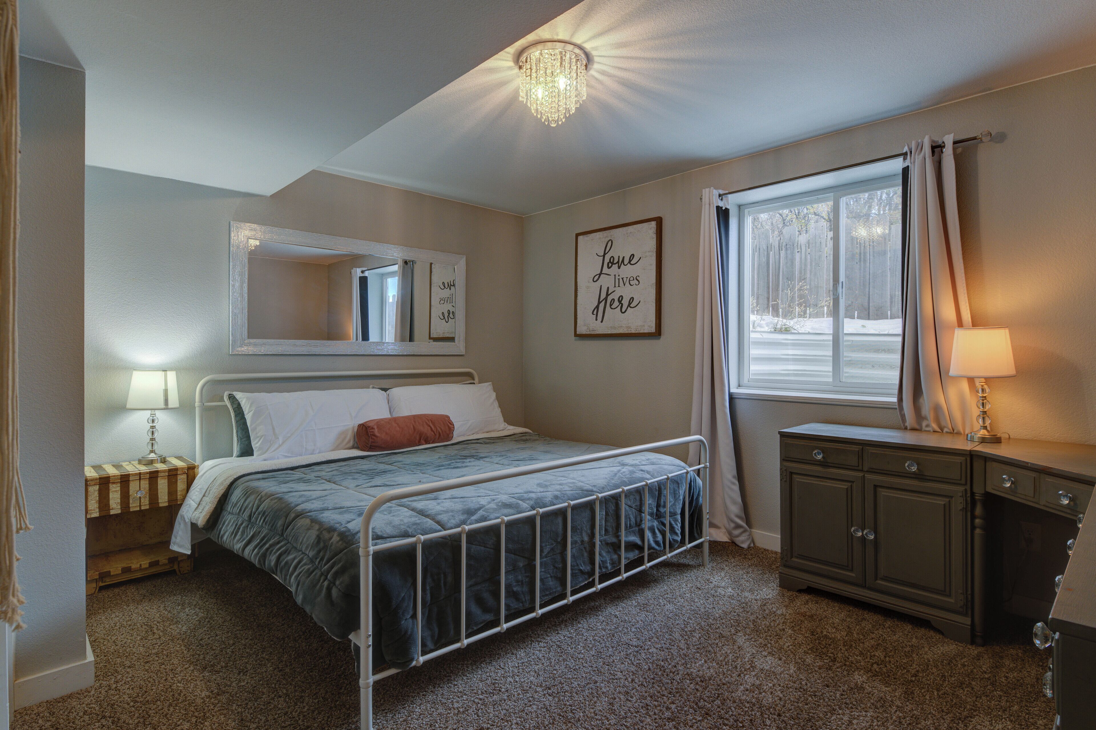 A bedroom with a bed, a nightstand, a dresser, a mirror, and a window with curtains.